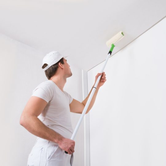 A painter painting ceiling with long roller.