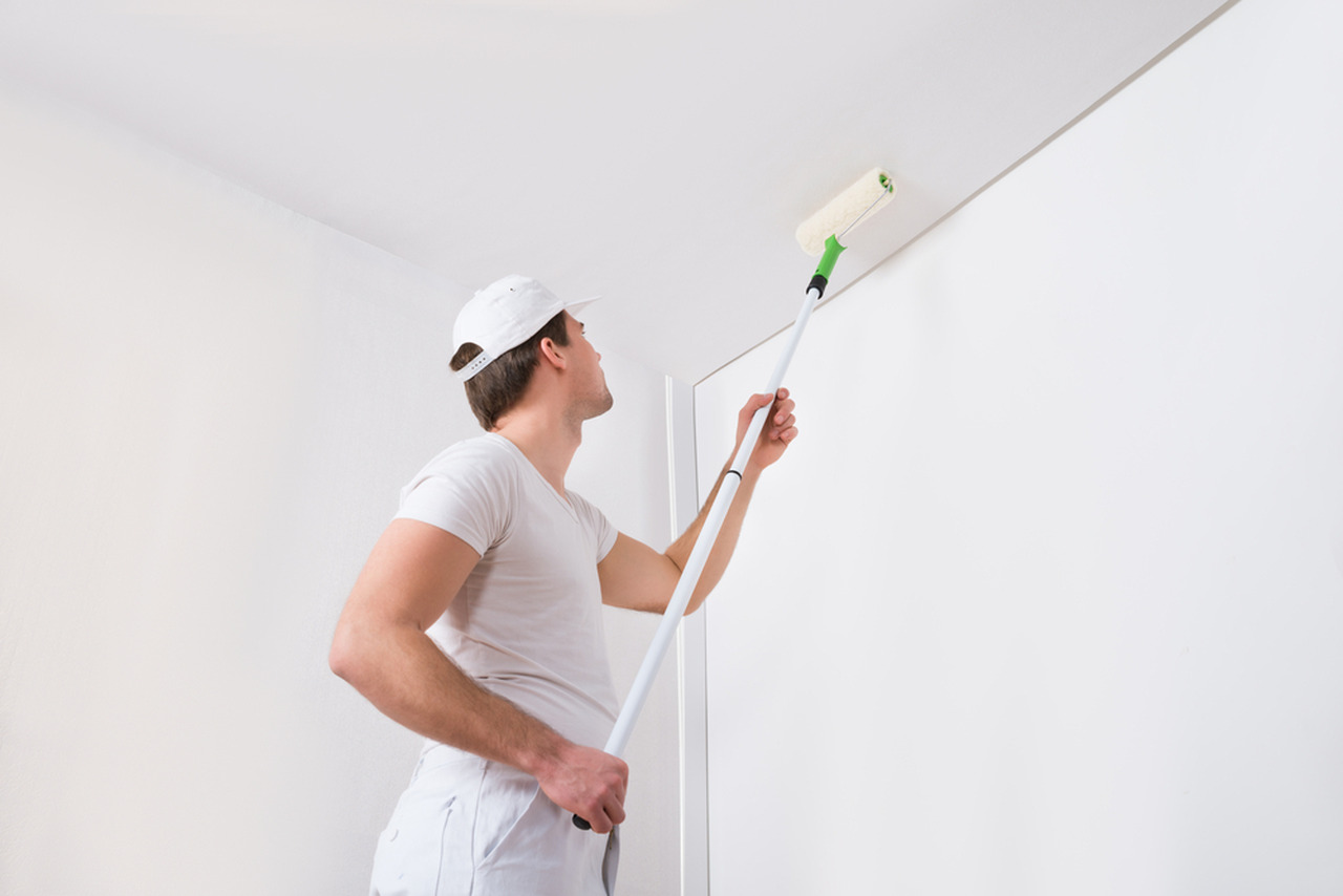 A painter painting ceiling with long roller.