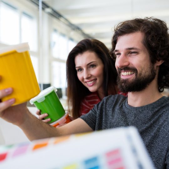 A man and women holding and looking at Eco-Friendly paint buckets in yellow and green colors.