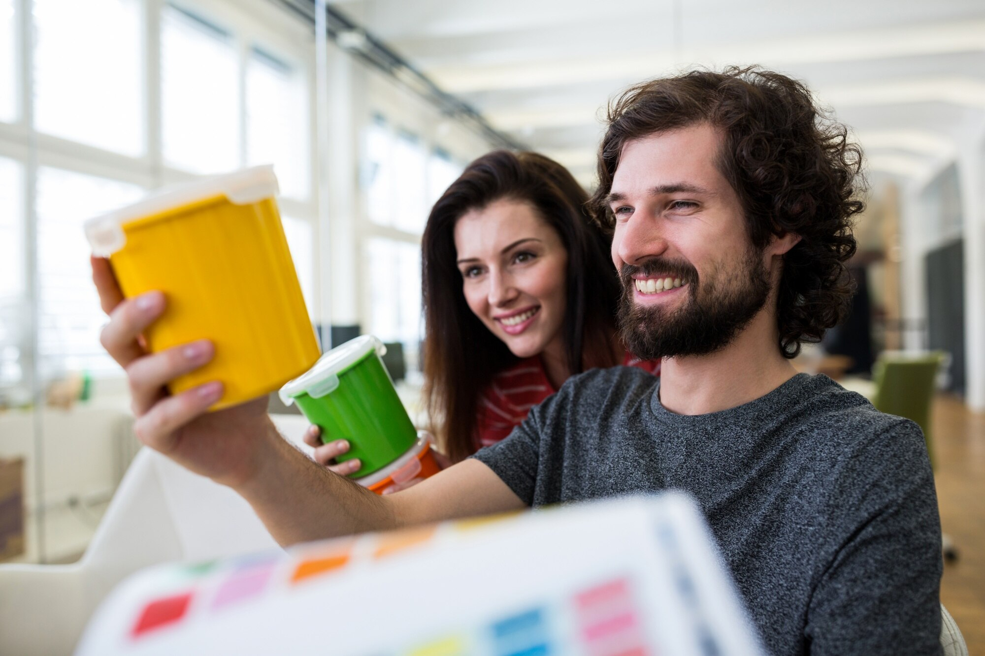 A man and women holding and looking at Eco-Friendly paint buckets in yellow and green colors.