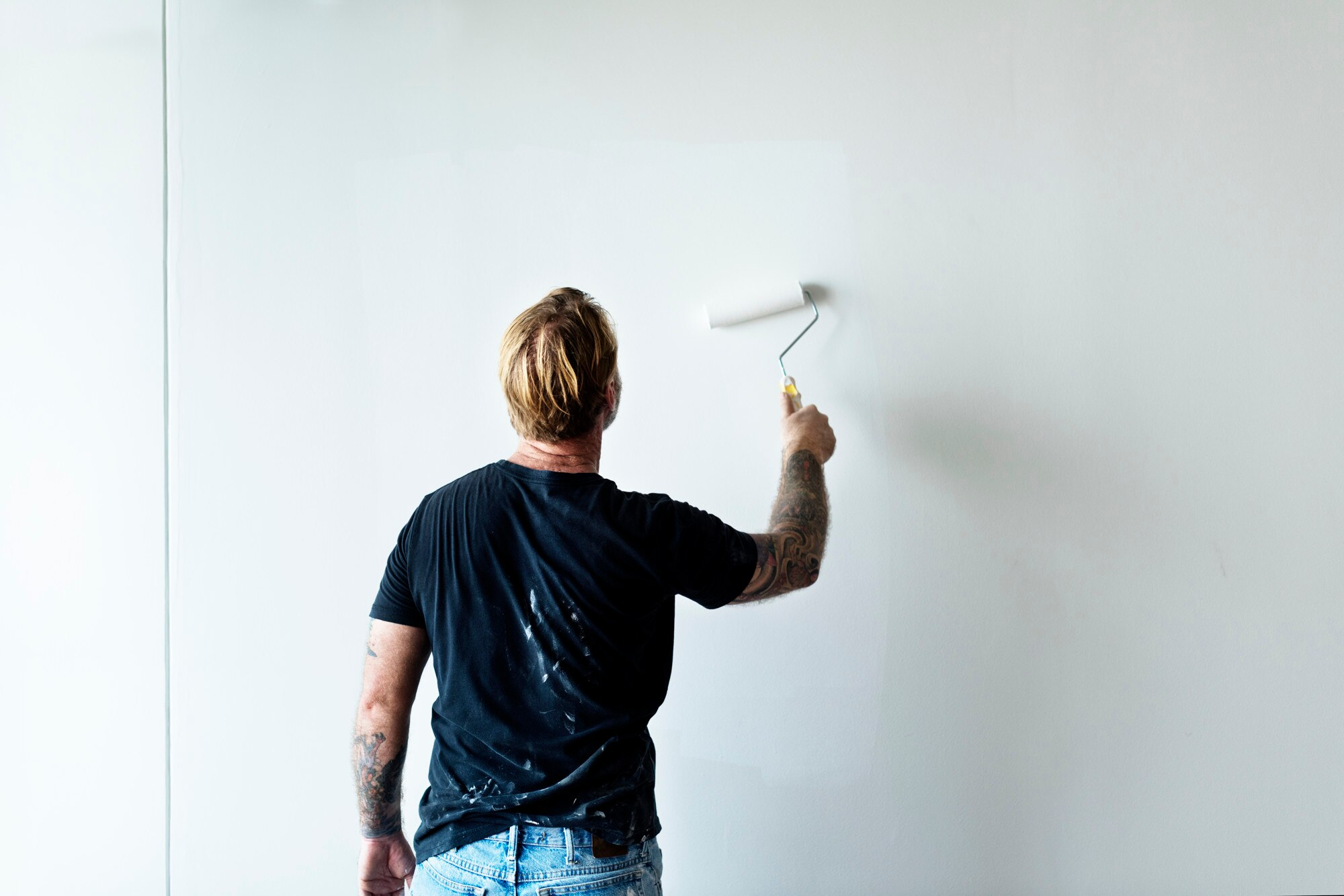 a man applying wall primer with a roller on a wall.