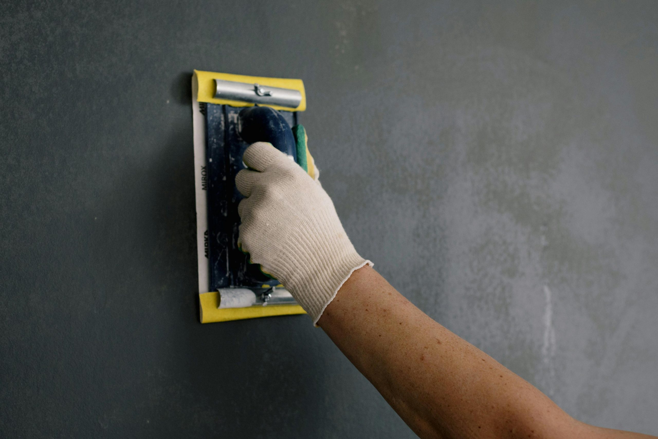 Close-up of a professional preparing a wall with a sanding tool, illustrating essential steps for wall preparation before painting.