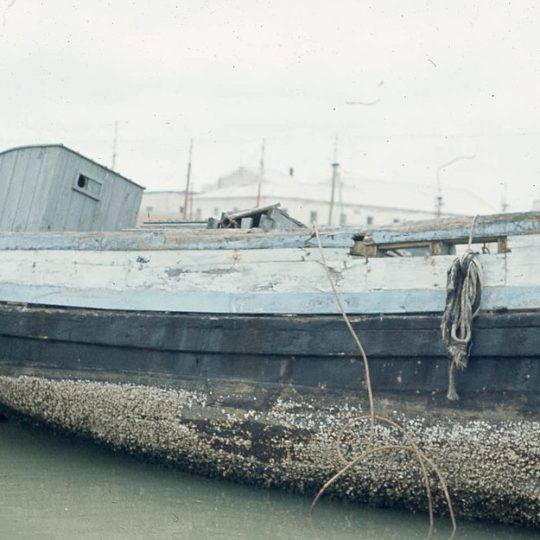 Old wooden boat with heavy barnacle buildup on the hull, showing the need for anti-fouling coatings to protect marine vessels.