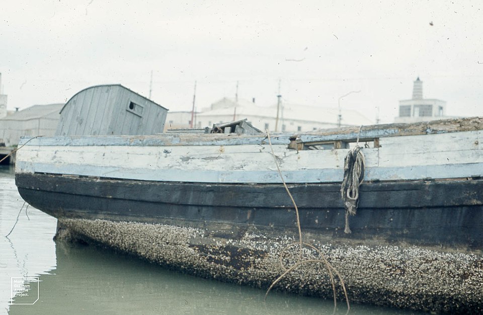 Old wooden boat with heavy barnacle buildup on the hull, showing the need for anti-fouling coatings to protect marine vessels.