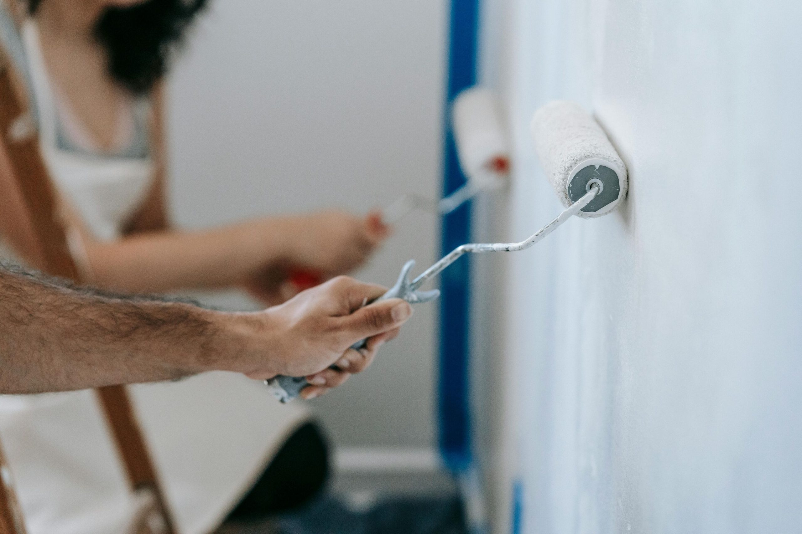 Close-up of people using paint rollers to apply a fresh coat of white paint on a wall, representing easy-clean and washable wall paint solutions.