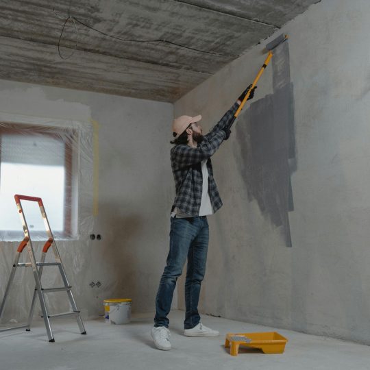 Worker applying industrial coatings to a factory wall using a paint roller, illustrating the process of choosing the right industrial coatings for Singapore factories.