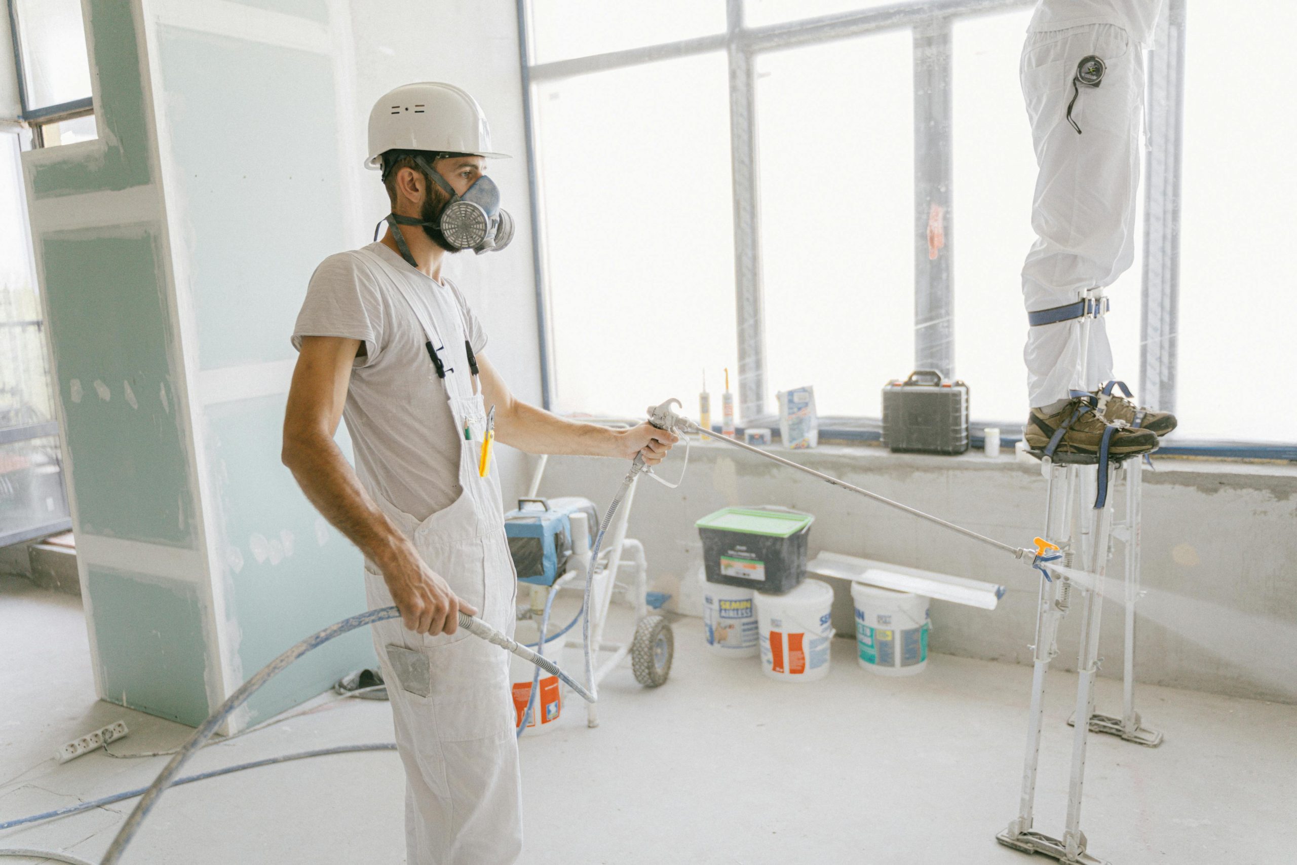 Industrial worker applying protective coatings with a spray gun inside a facility, showing how protective coatings reduce maintenance costs for industries.