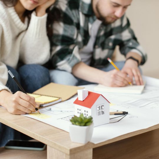 Couple planning a home renovation budget with house model and design sketches on the table.