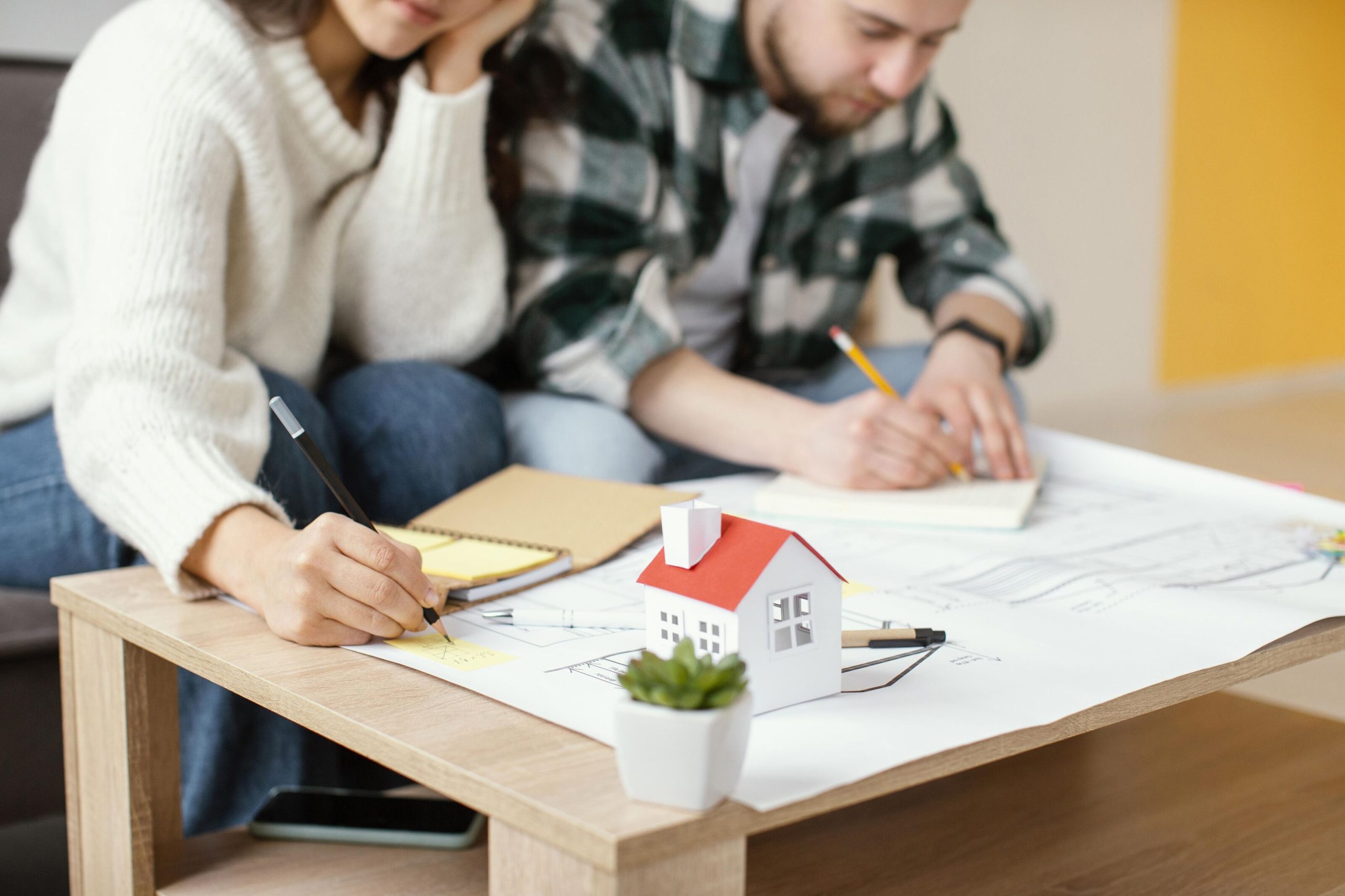 Couple planning a home renovation budget with house model and design sketches on the table.