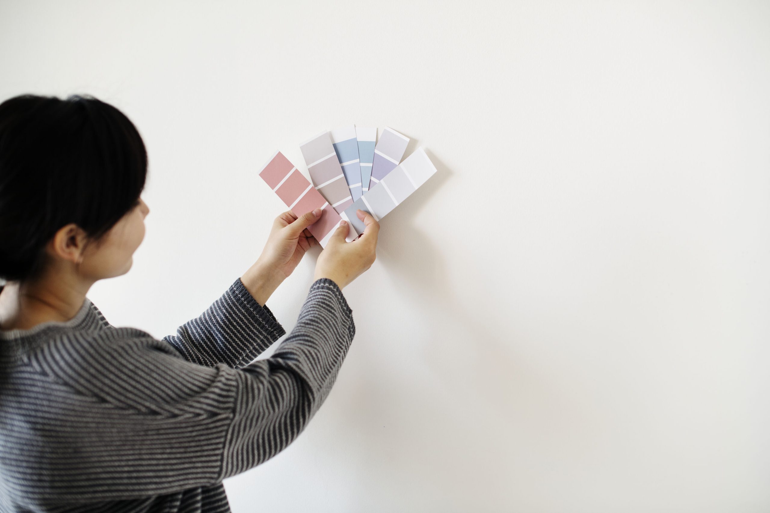 Person comparing paint colour swatches against a wall to choose modern colour palettes for home painting by Berger Paints.