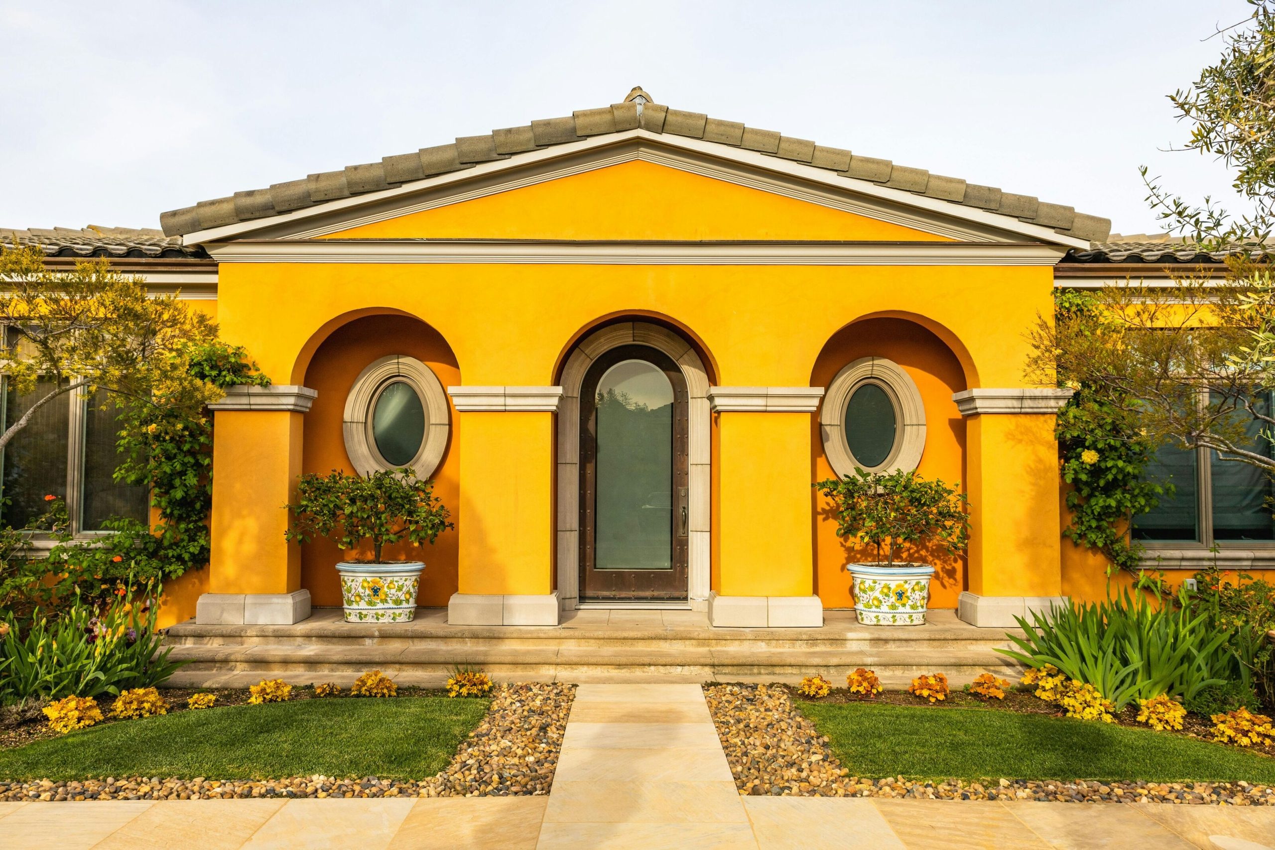 Bright yellow house exterior with arched windows and landscaped garden, illustrating exterior repainting ideas and paint selection for homes in Singapore in 2026.