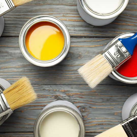 Paint cans and paint brushes on wooden surface for online vs offline paint buying in Singapore 2026.