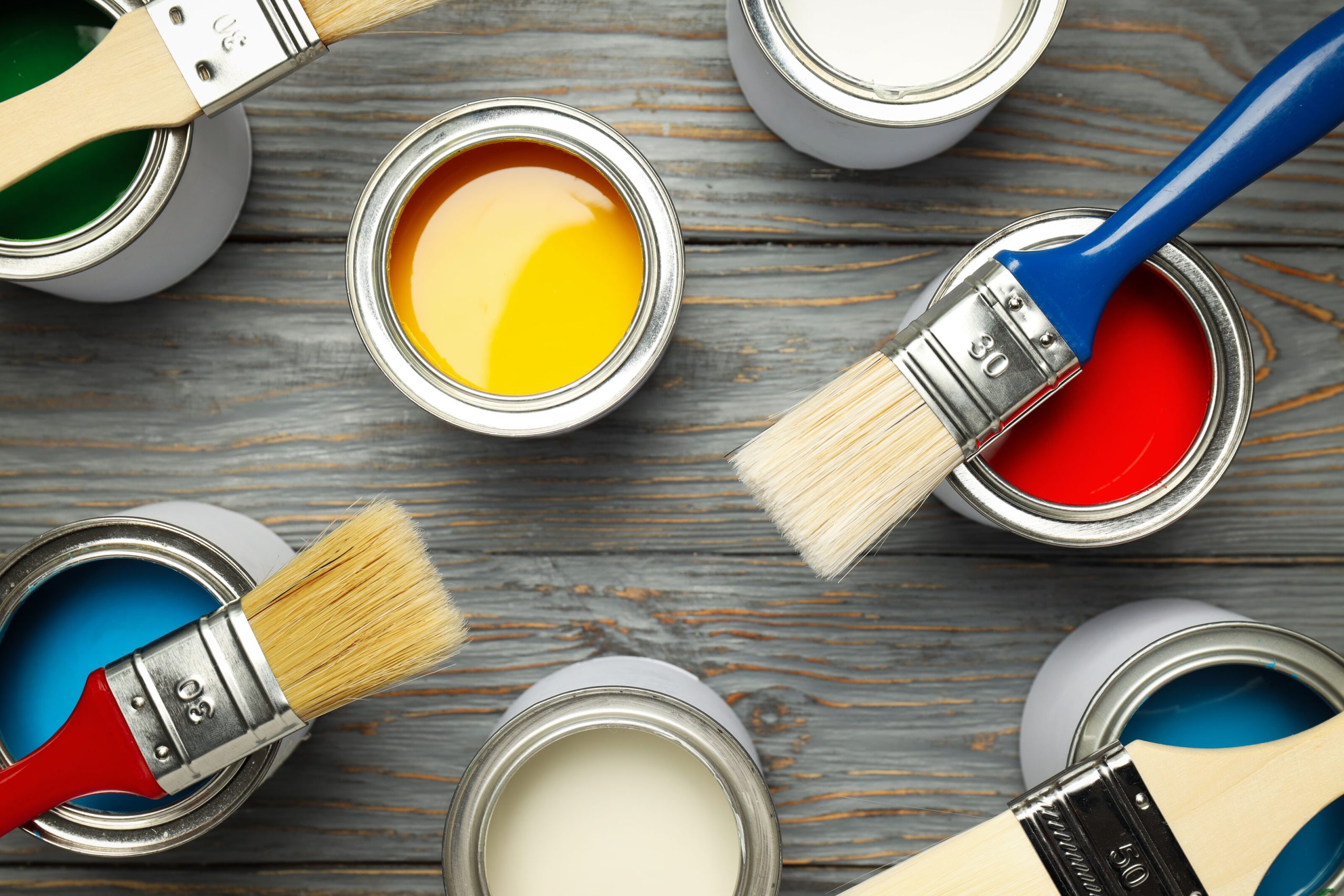 Paint cans and paint brushes on wooden surface for online vs offline paint buying in Singapore 2026.